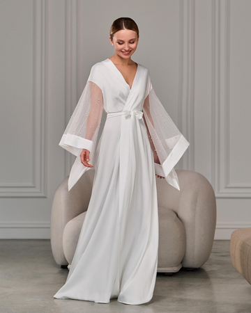 Bride in long white satin robe with pearl-detailed sheer sleeves standing gracefully