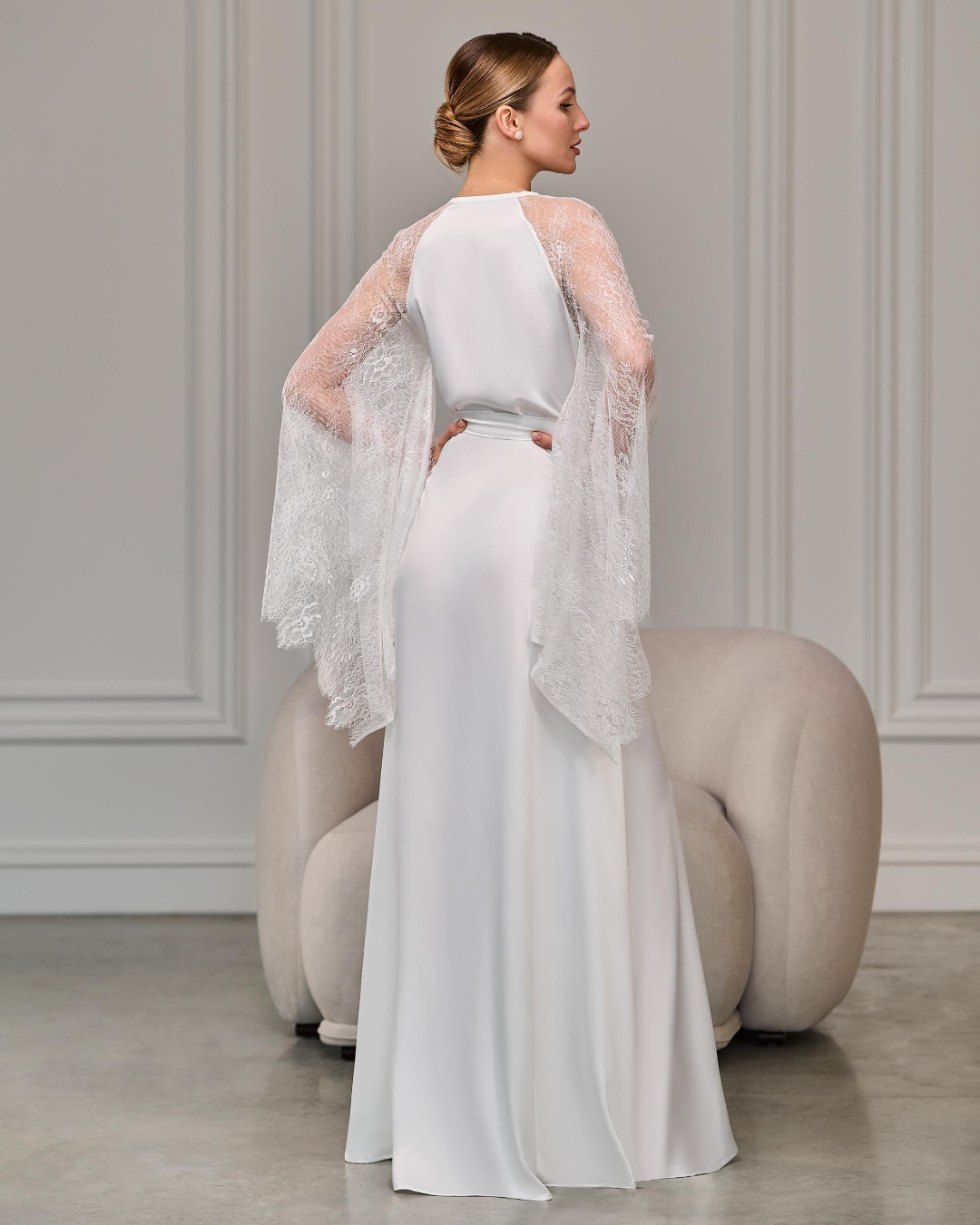 Bride in ivory satin robe with lace raglan sleeves standing