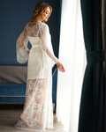 a woman in a white lace robe standing in front of a window