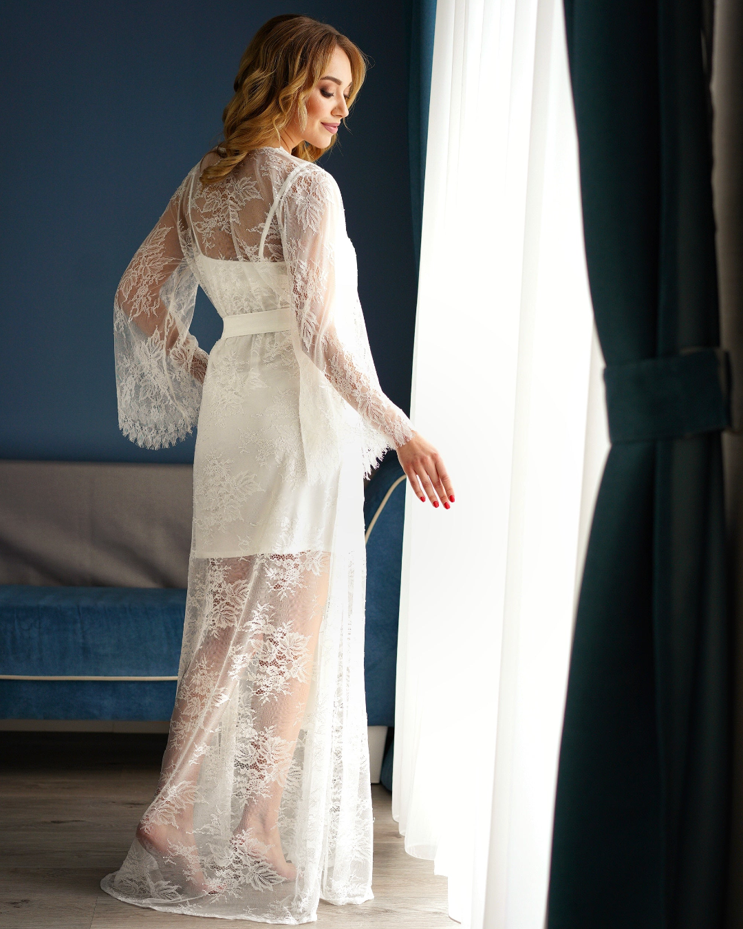 a woman in a white lace robe standing in front of a window