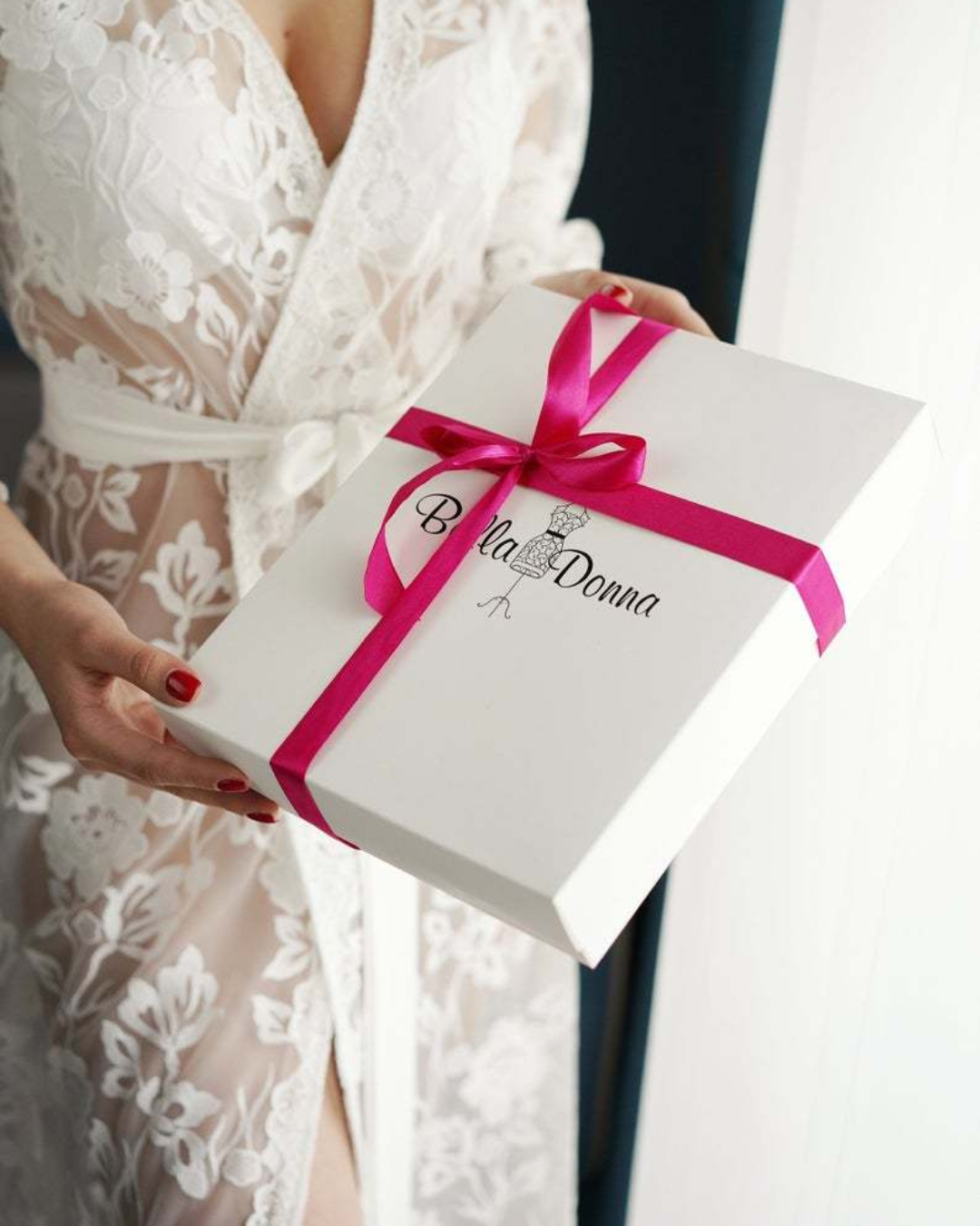 a woman holding a white box with a pink ribbon