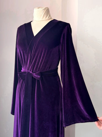 Hand holding wide sleeve of purple velvet robe showing elegant soft texture and flow.