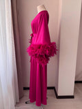 A mannequin wearing a long, pink dress with a feathery trim, displayed in a room with white walls and a window.
