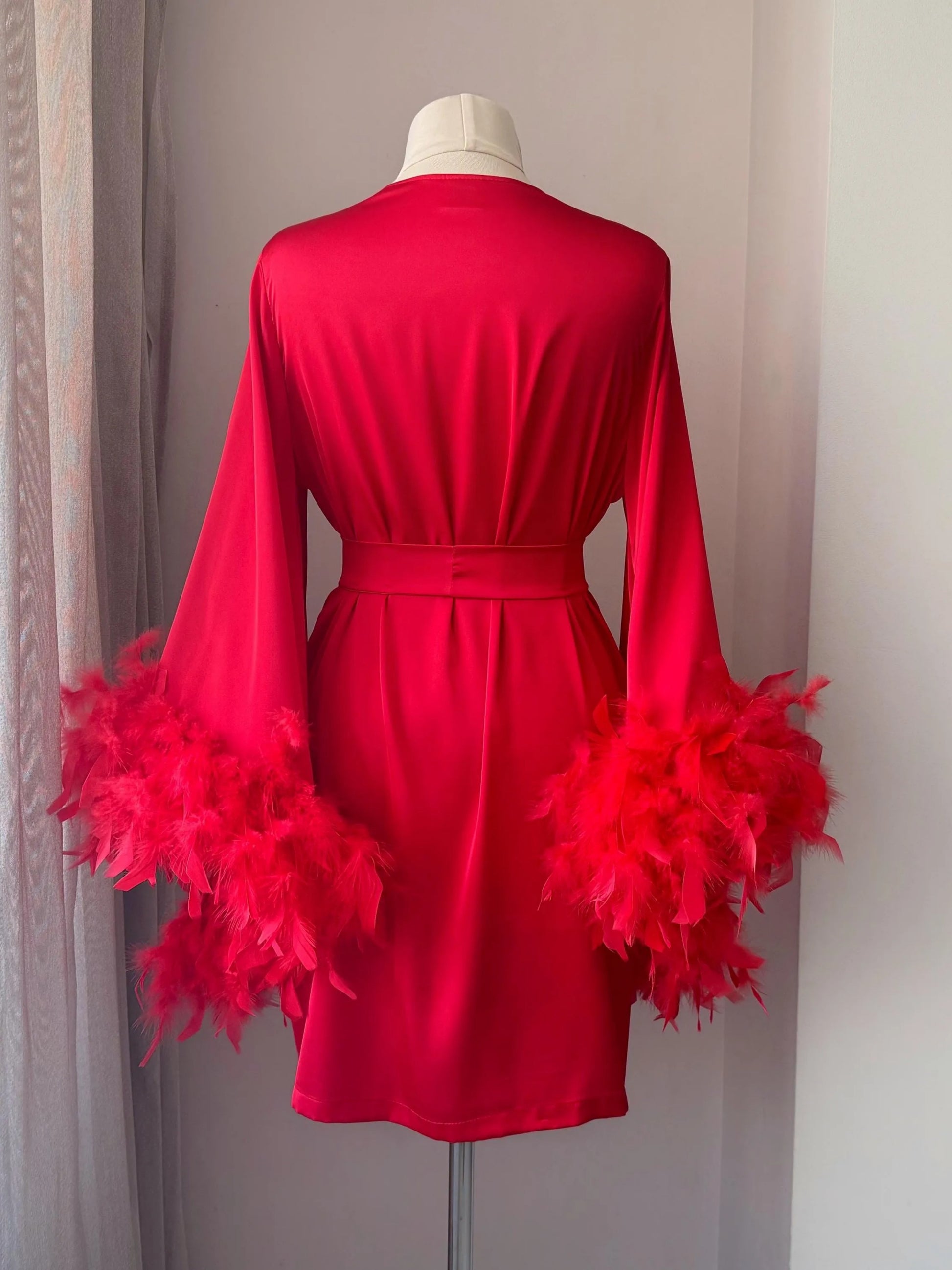 A red kimono with long sleeves and feather details displayed on a mannequin.