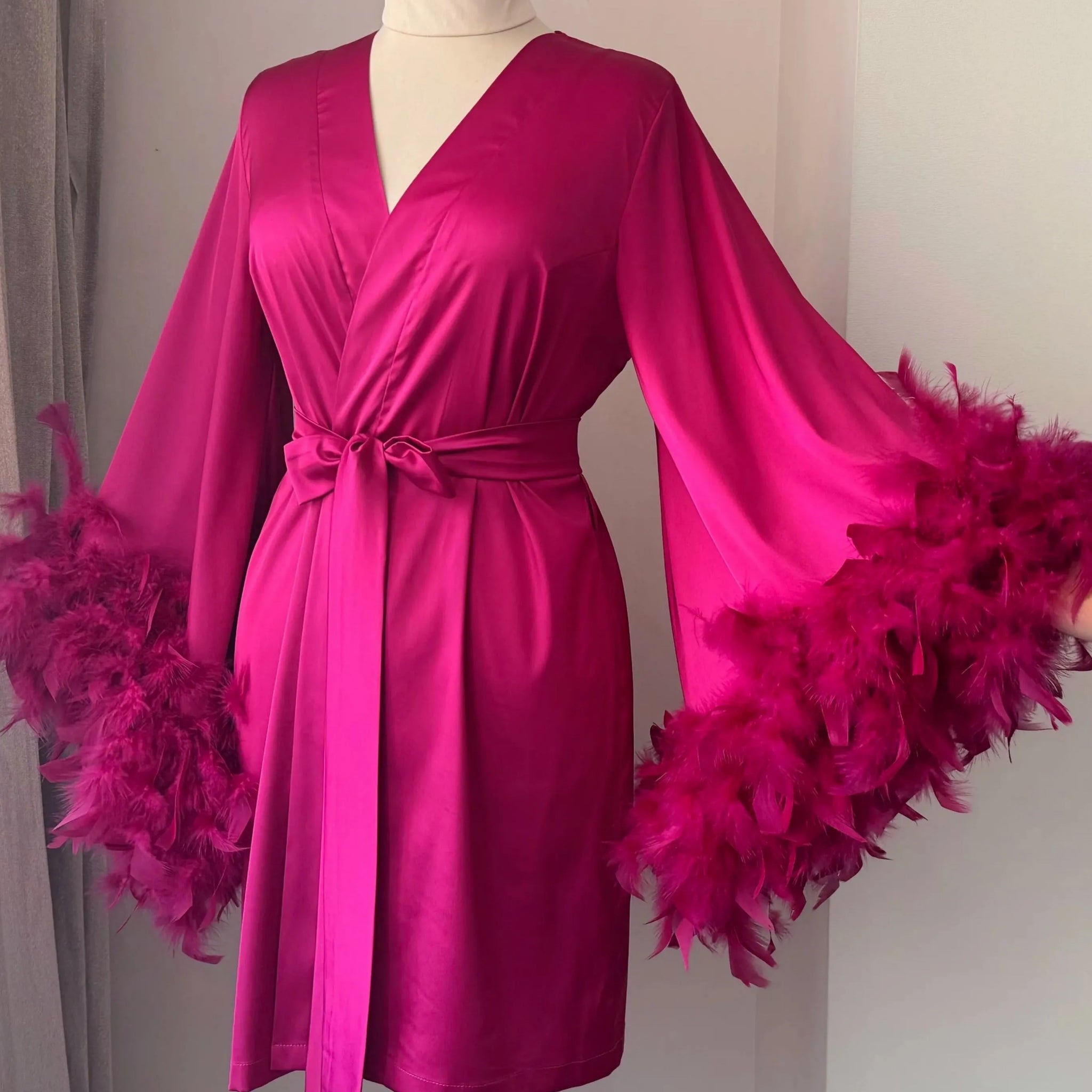 A mannequin wearing a bright pink satin robe with feather accents, displayed on a mannequin stand.