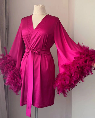 A mannequin wearing a bright pink satin robe with feather accents, displayed on a mannequin stand.