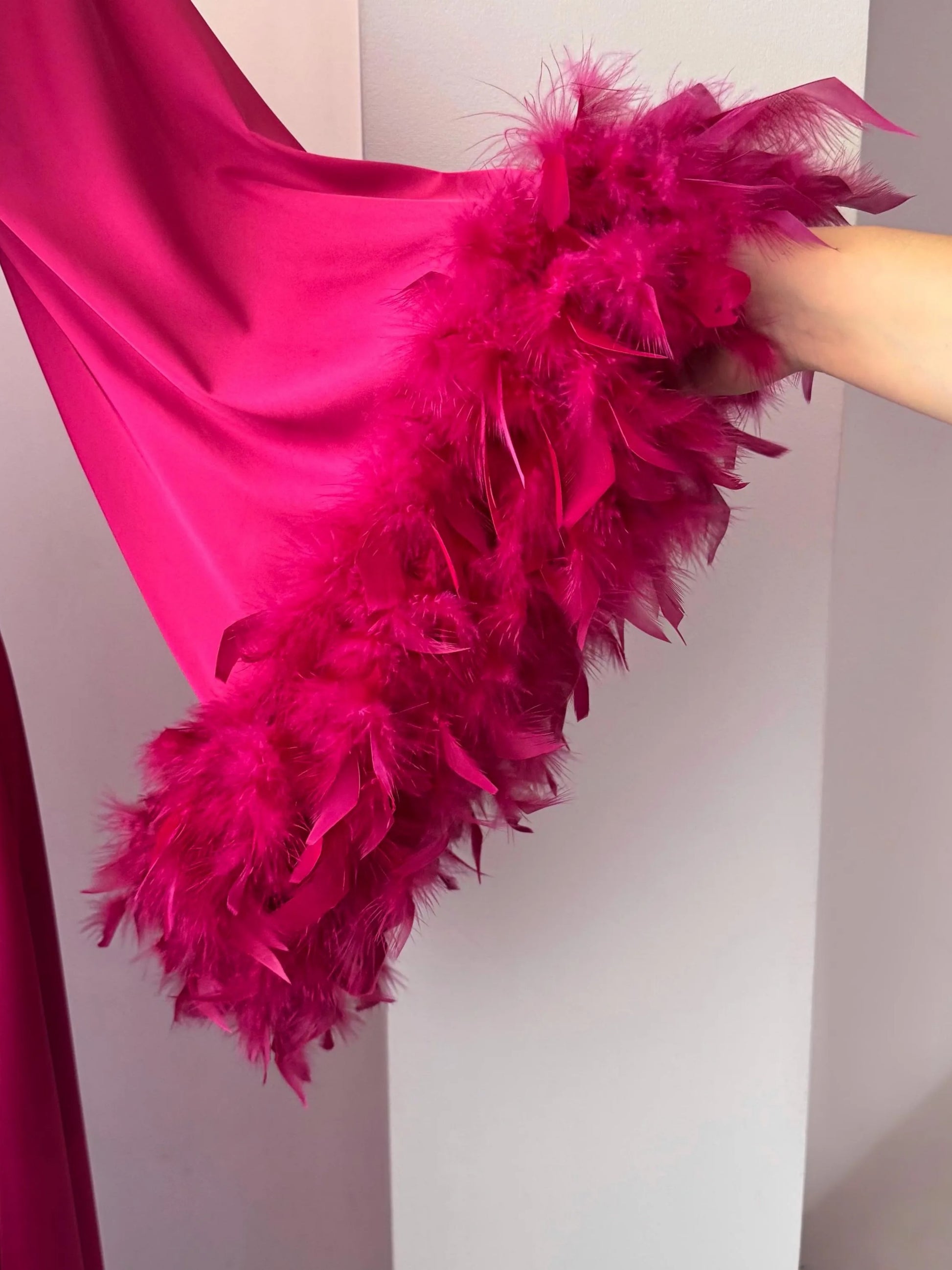 A close-up view of a person's arm wearing a vibrant pink feathered garment, with the feathers appearing to be made of real feathers.