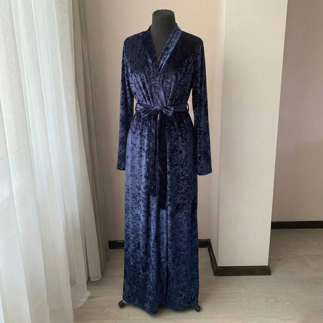 Woman wearing a long midnight blue crushed velvet robe in a floor-length wrap silhouette