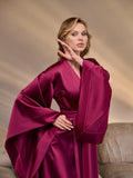 Close-up of a woman in a dark burgundy satin kimono robe with wide structured sleeves, highlighting the smooth sheen, intricate stitching, and designer belt for high-end bridal loungewear.