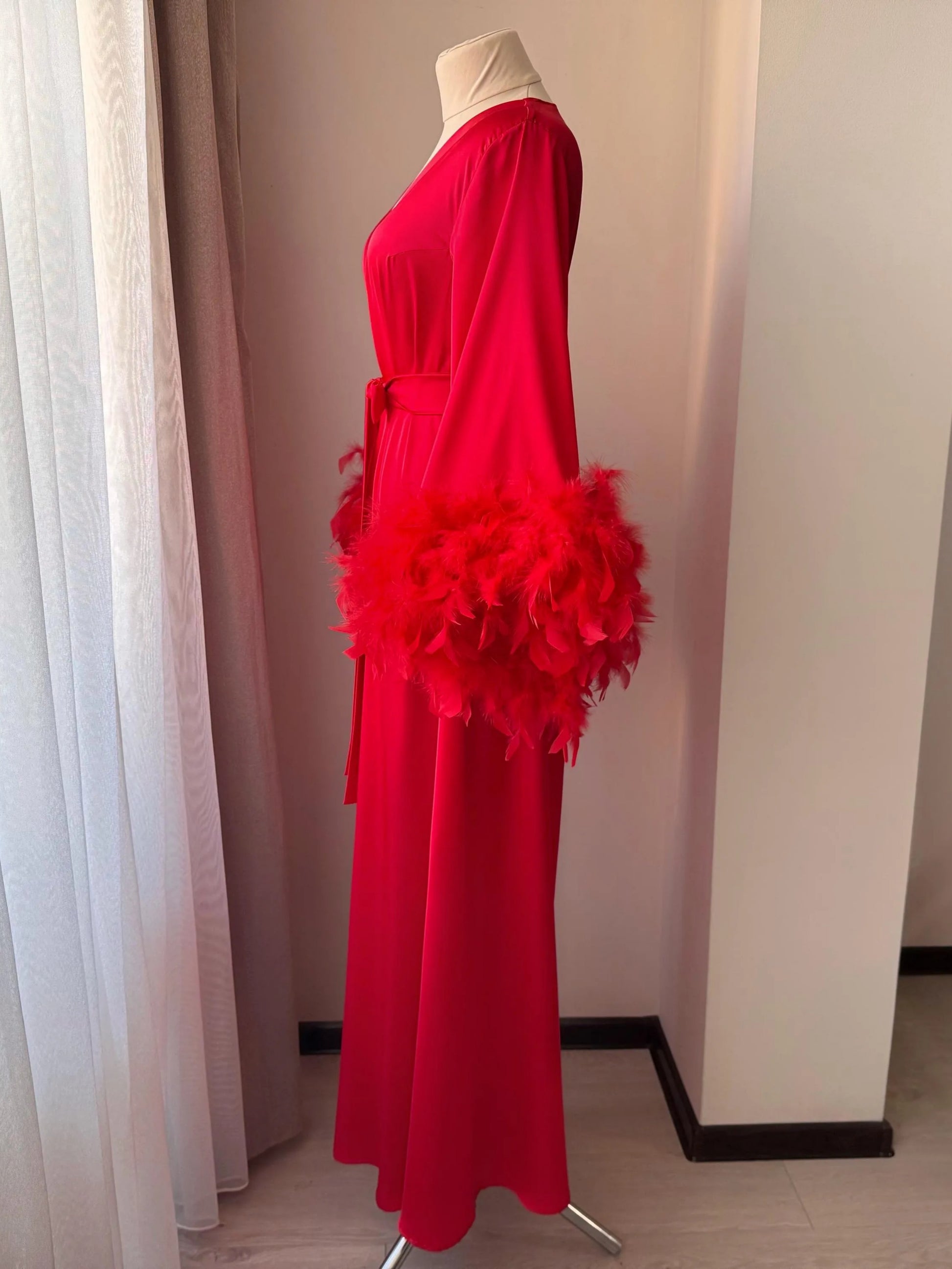 A mannequin wearing a long red dress with a large feather boa draped over the shoulder.