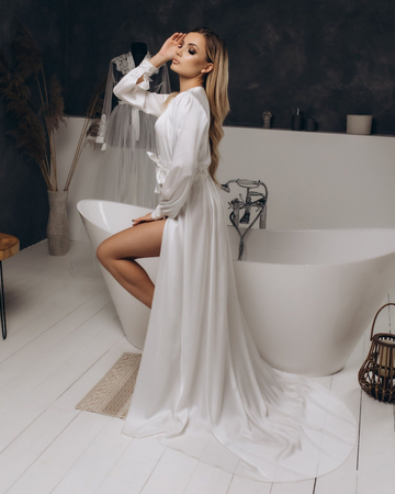 Long white satin bridal robe with train, worn by model sitting on tub edge, perfect for wedding day prep or boudoir photo shoot