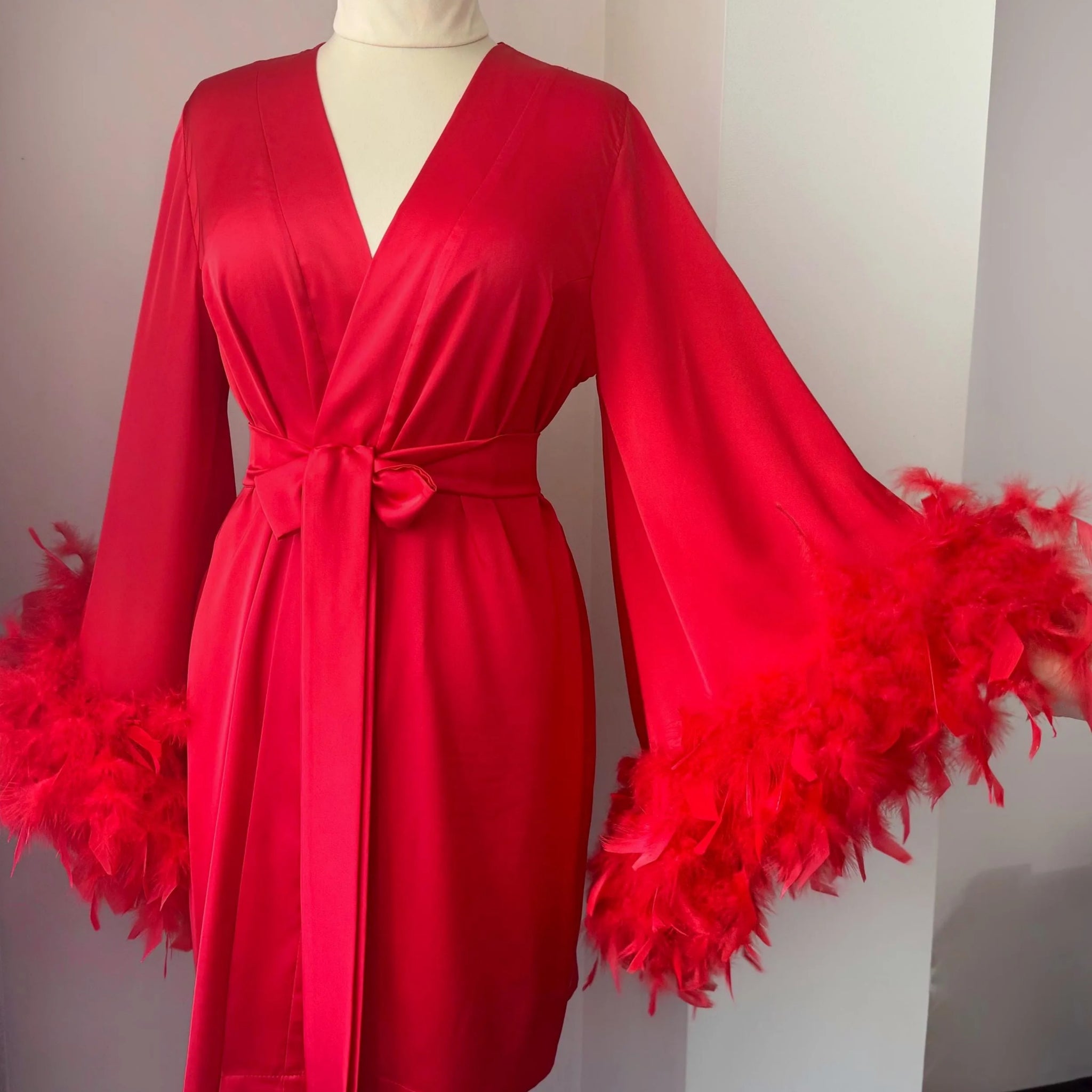 A red satin robe with long sleeves and feather accents displayed on a mannequin.