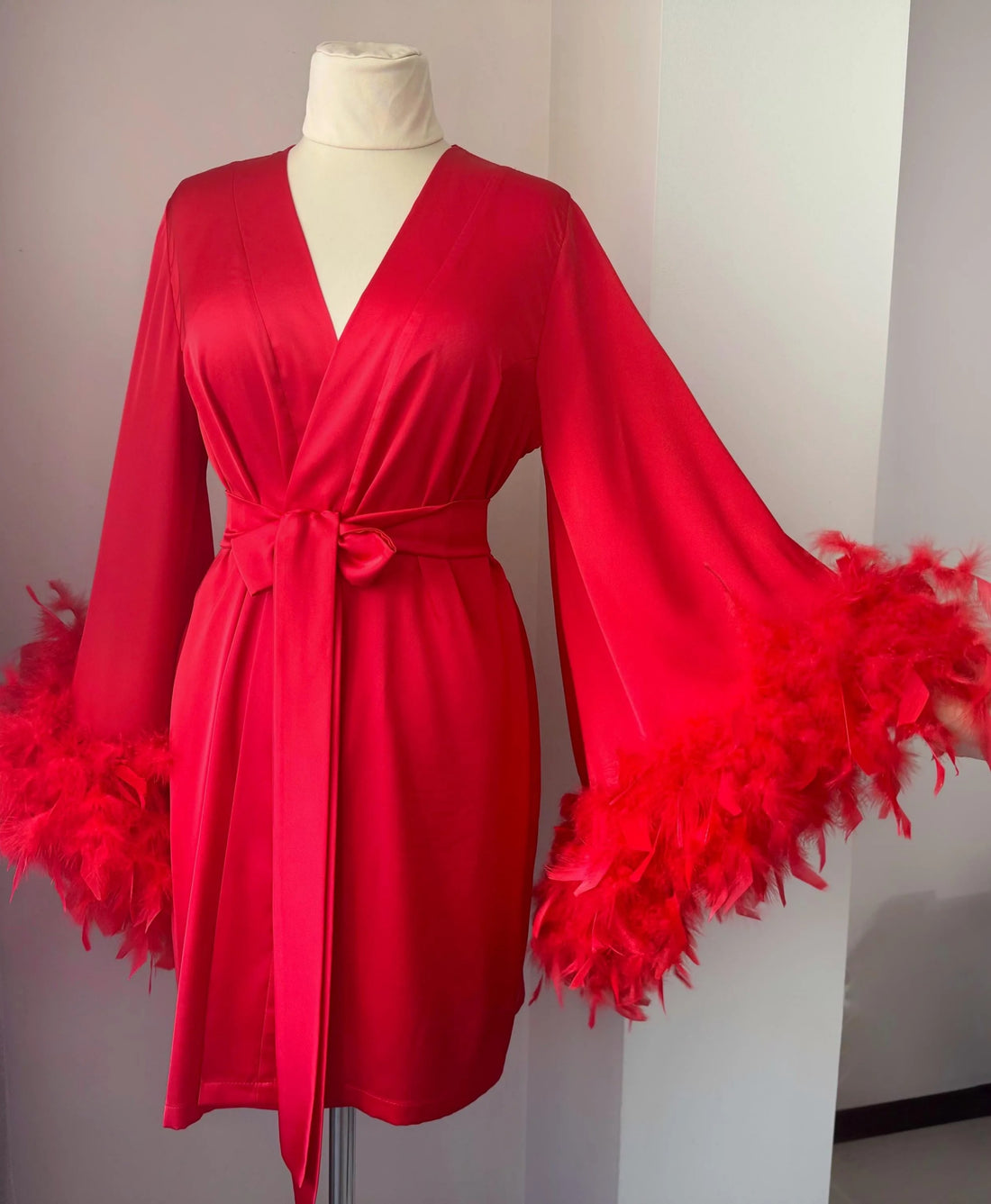 A red satin robe with long sleeves and feather accents displayed on a mannequin.