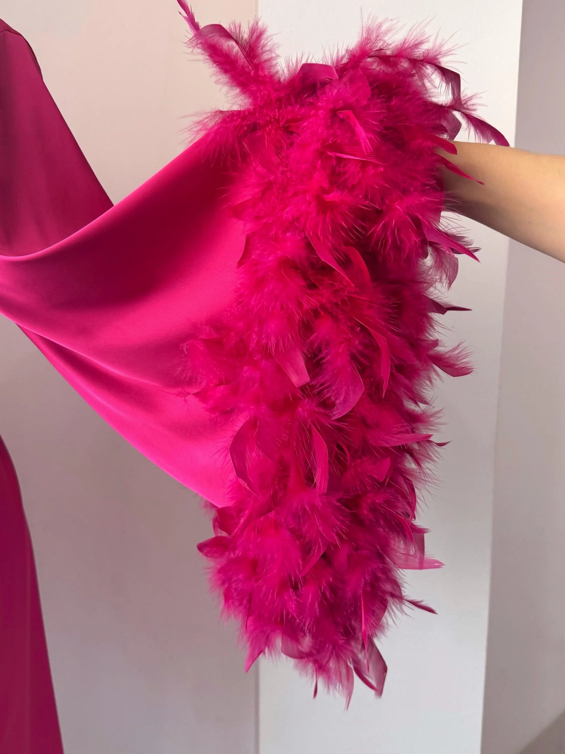 A close-up view of a vibrant pink feathered accessory, such as a shawl or cape, with a large amount of feathers attached to it.