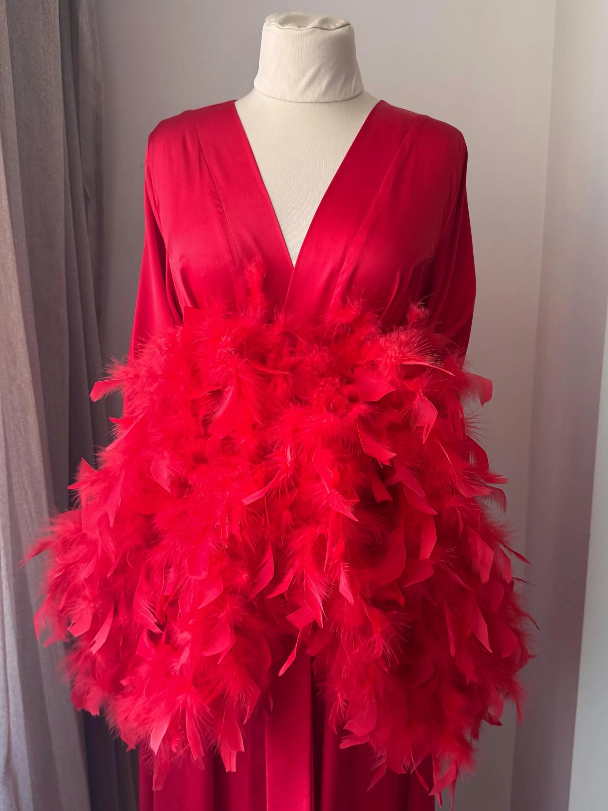 A mannequin wearing a vibrant red dress with a large, fluffy feather boa draped over the front.
