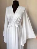 A mannequin wearing a white satin robe with long sleeves and a bow at the waist.