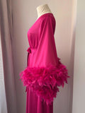 A mannequin wearing a long pink dress with a large feathered cape draped over the shoulder.