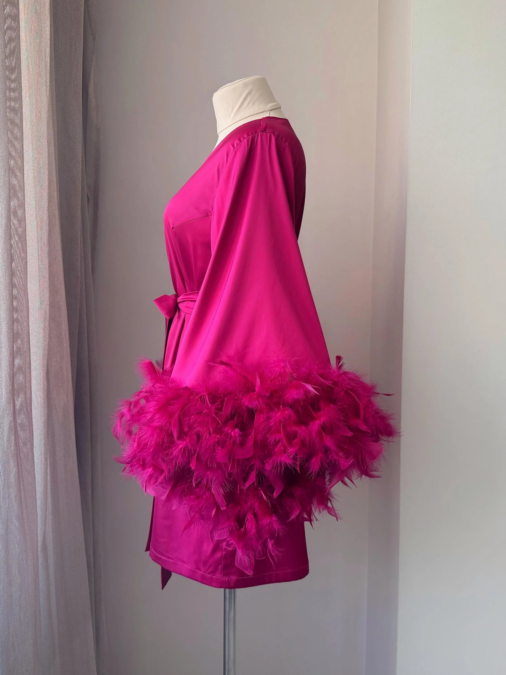 A mannequin wearing a bright pink dress with a large feathered cape draped over it.