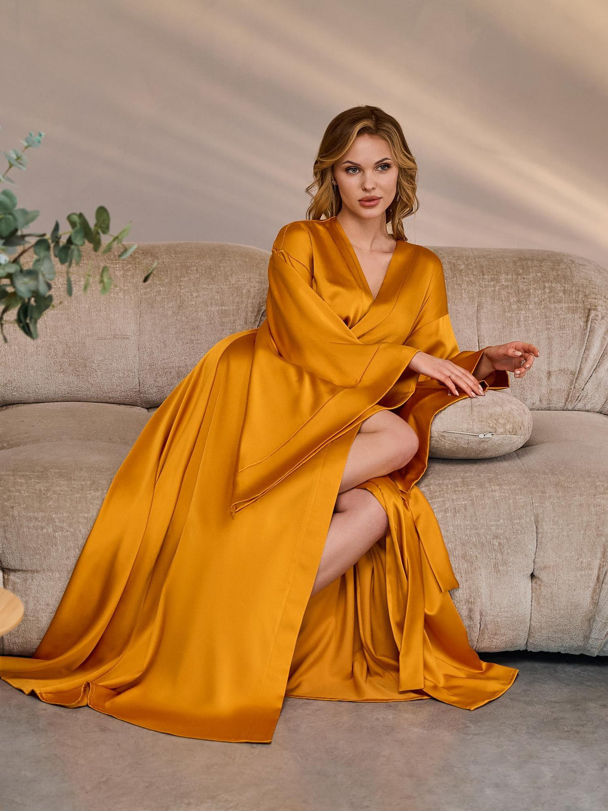Model seated on a sofa in a long golden mustard silk satin robe