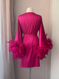 A mannequin wearing a bright pink robe with long sleeves and feather details on the sleeves.