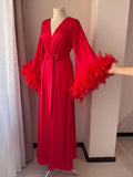 A mannequin wearing a long, red robe with feather sleeves and a bow at the waist.