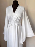 A mannequin wearing a white satin robe with long sleeves and a bow at the waist.
