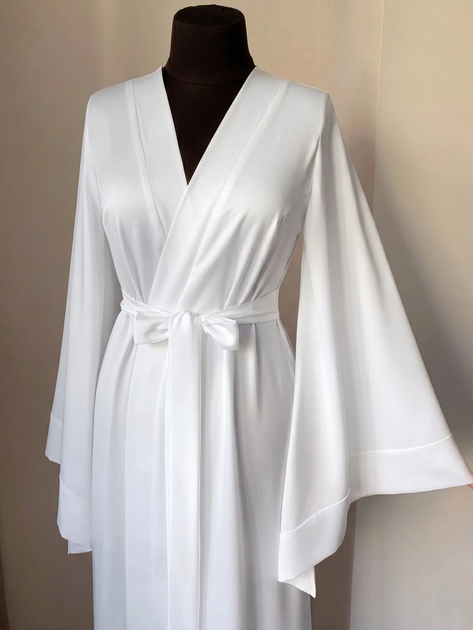A mannequin wearing a white satin robe with long sleeves and a bow at the waist.