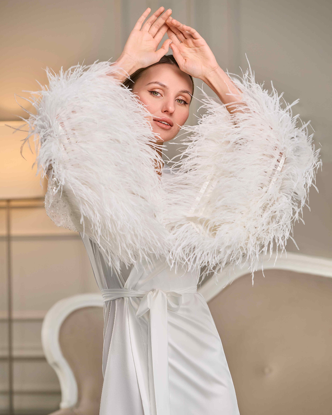 Close-up of bride in ostrich feather bridal robe, arms raised, highlighting fluffy feather sleeves
