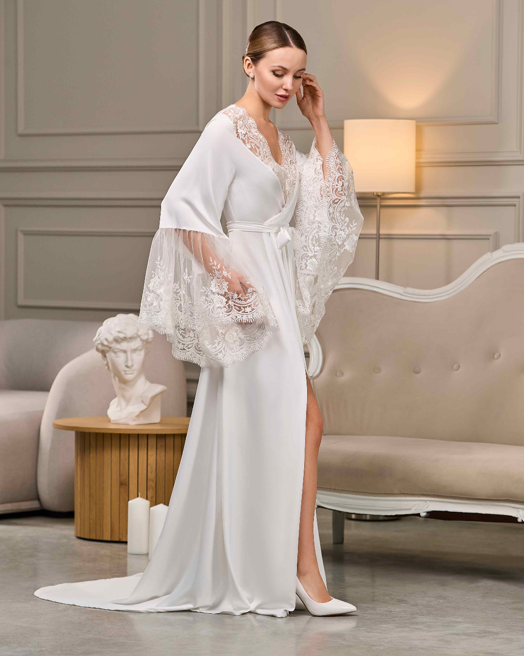 White bridal robe with dramatic lace bell sleeves and slit, worn by a bride in a graceful pose