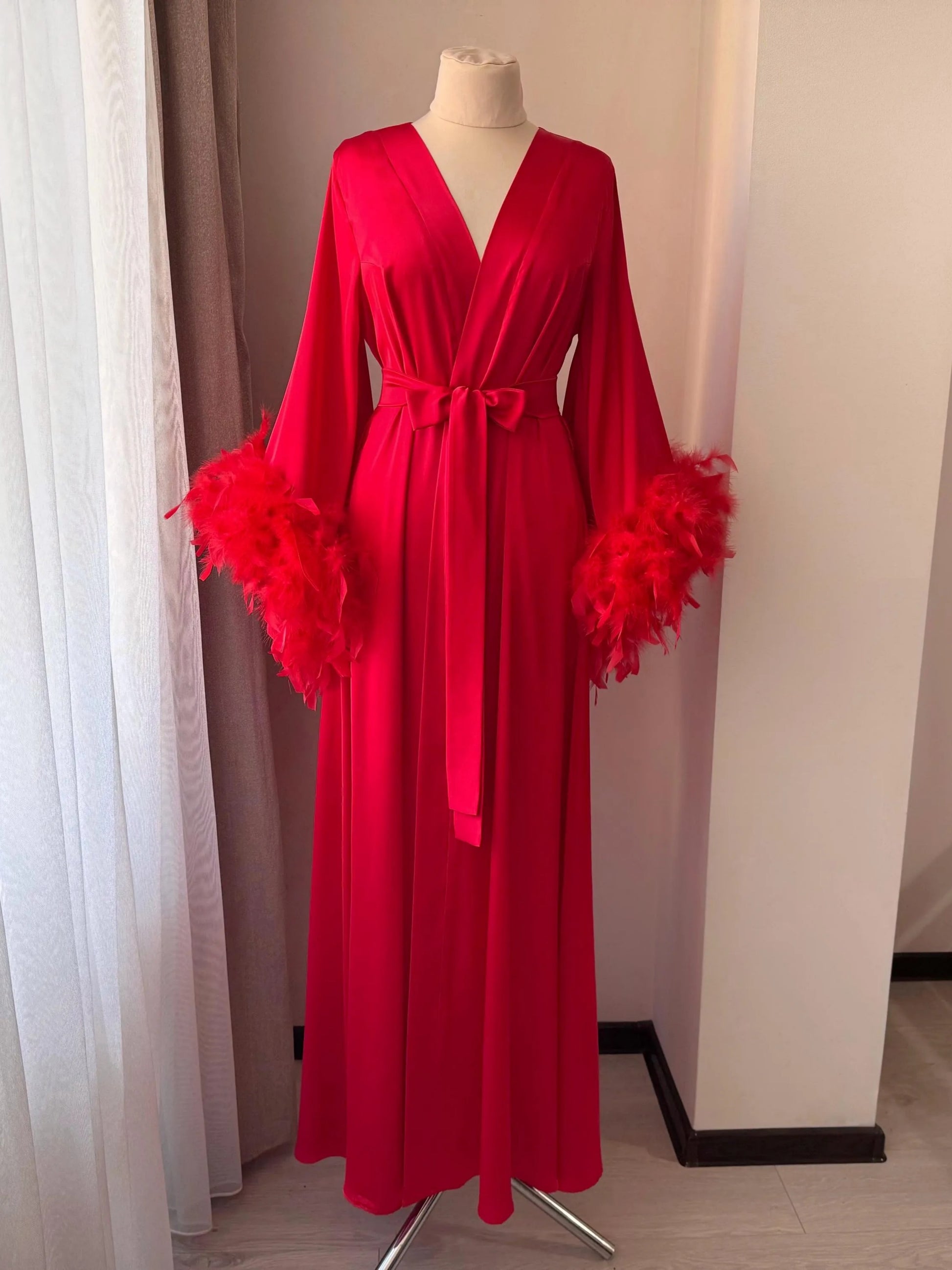 A red satin robe with long sleeves and feather accents, displayed on a mannequin.