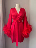 A red satin kimono with long sleeves and feather accents displayed on a mannequin.