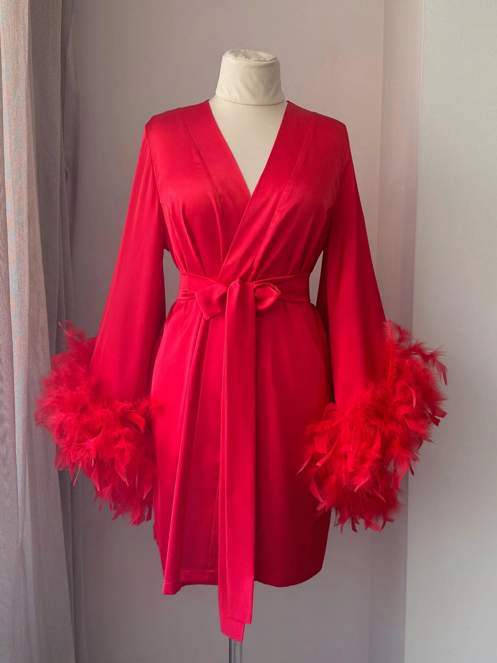 A red satin kimono with long sleeves and feather accents displayed on a mannequin.