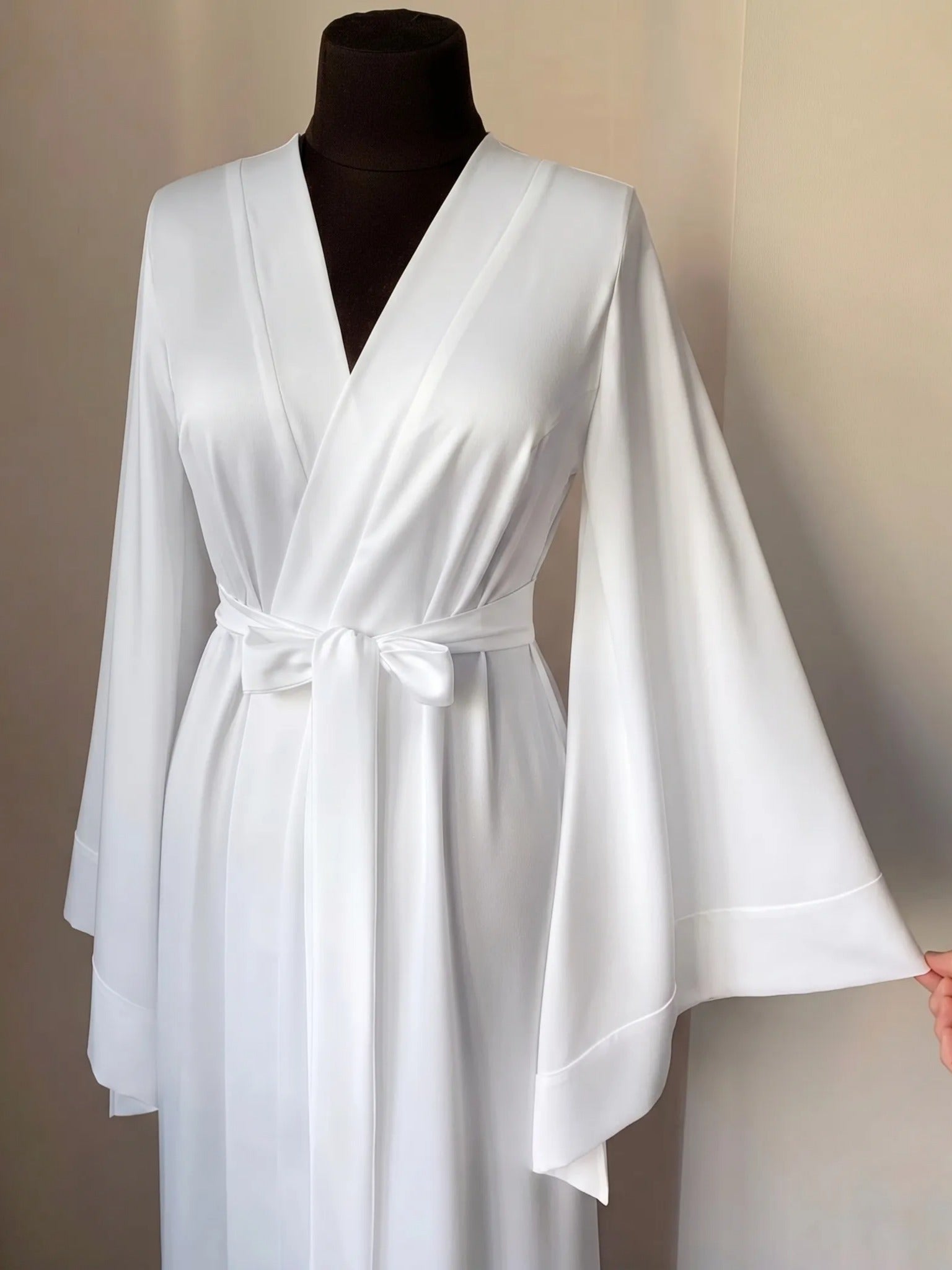 A mannequin wearing a white satin robe with long sleeves and a bow at the waist.