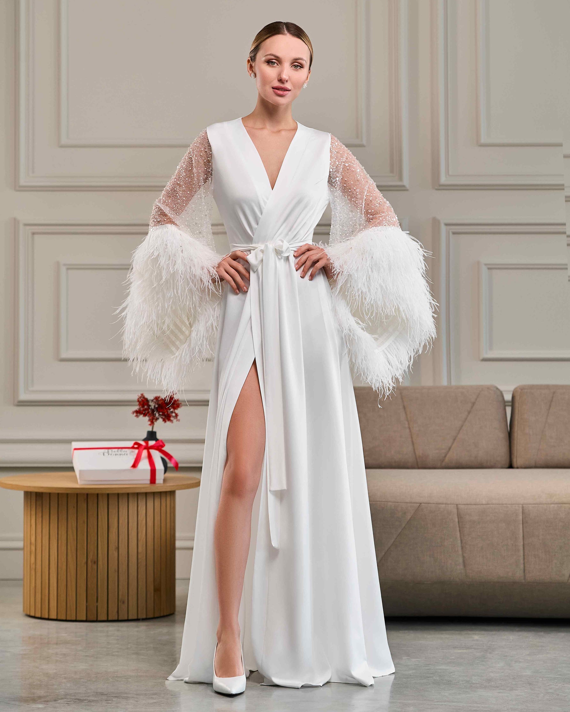 Bride wearing long white robe with sheer beaded sleeves and voluminous ostrich feathers at the cuffs
