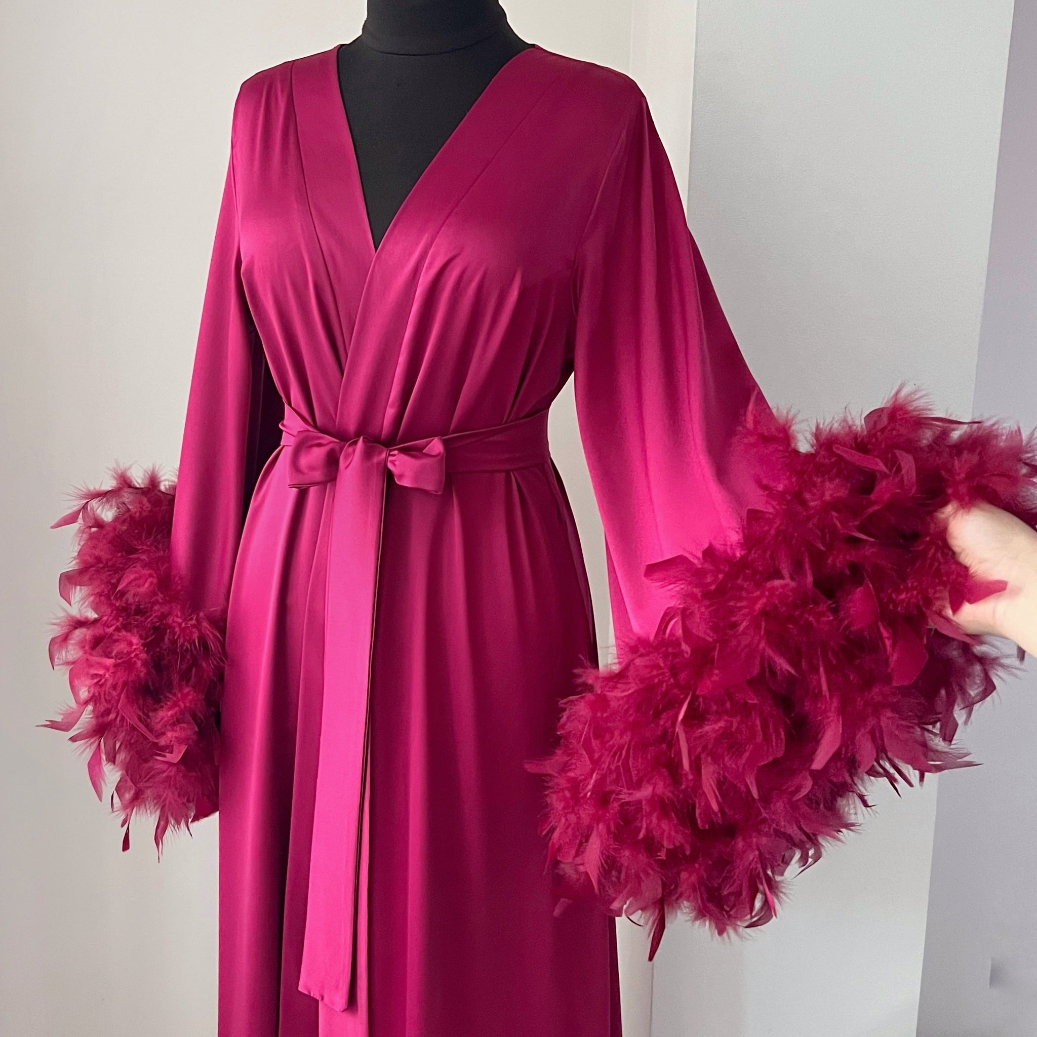 Pink dress with feathered sleeves on a mannequin against a white background