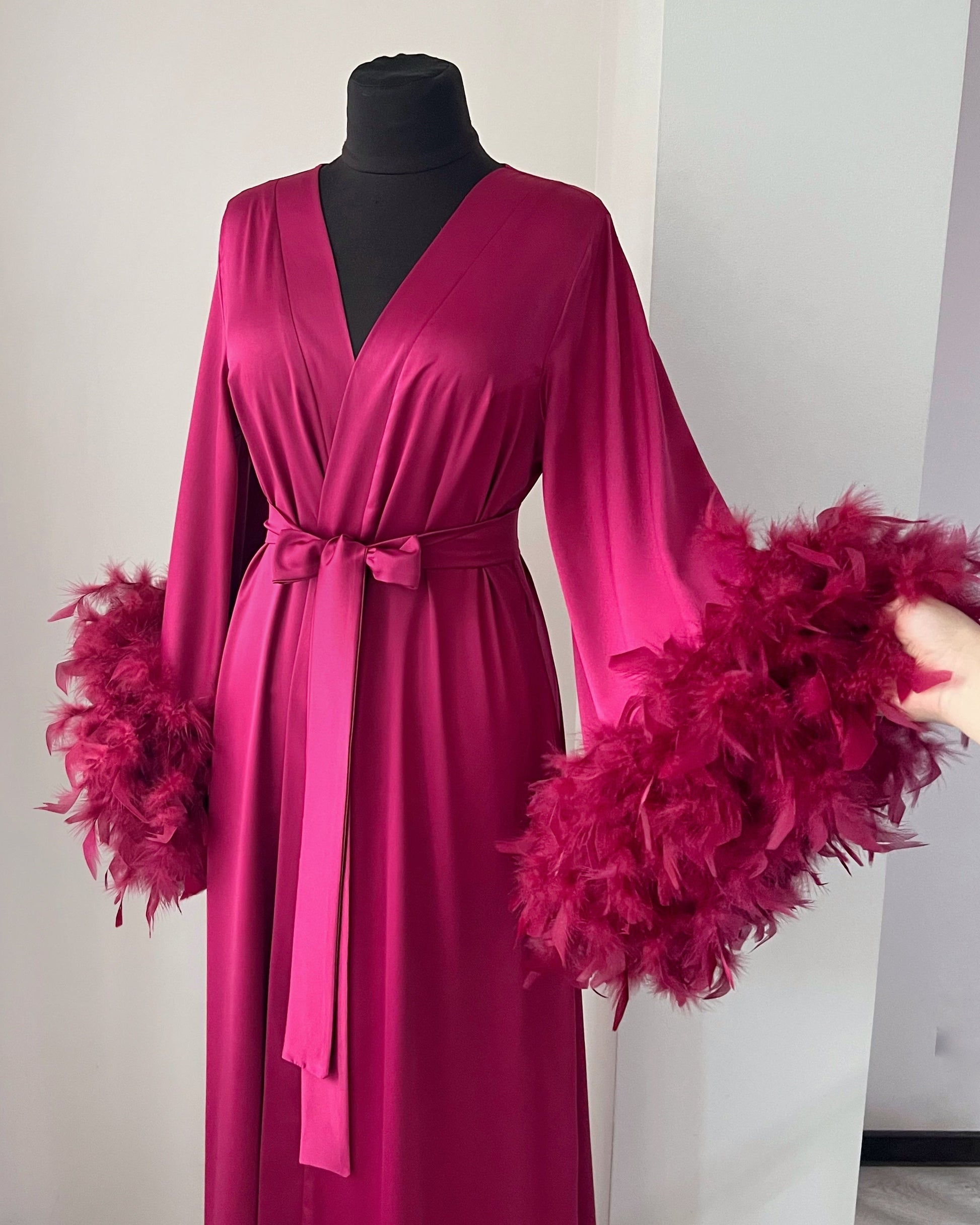 Pink dress with feathered sleeves on a mannequin against a white background