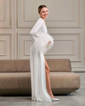 Side view of long ivory robe with ostrich feather details, model smiling in elegant bridal pose