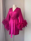 A mannequin wearing a bright pink satin robe with long sleeves and feather accents.