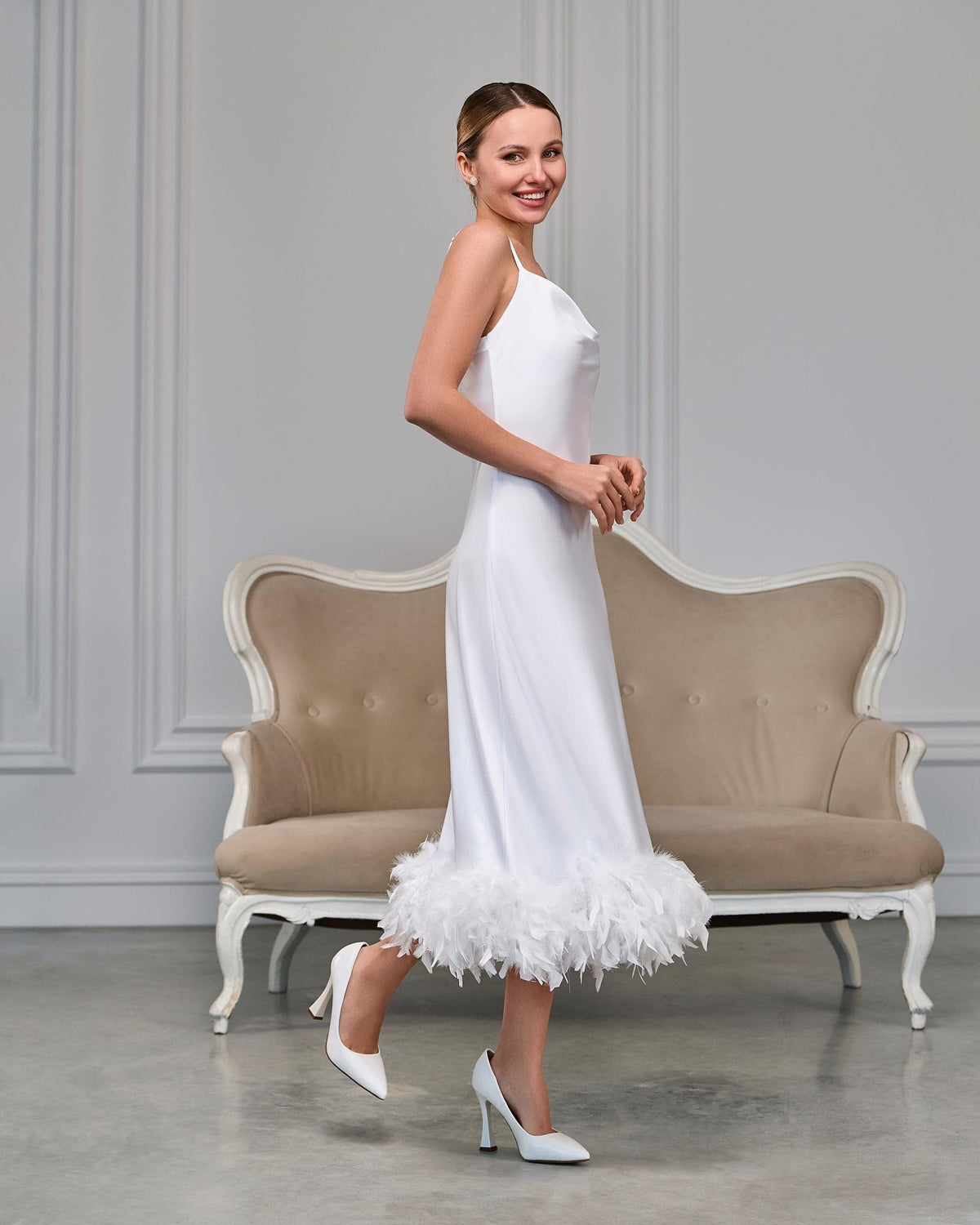 White satin bridal slip dress with draped cowl neckline and feather trim at the midi hem