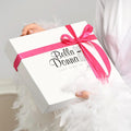 A person is holding a white gift box with a pink ribbon and the text 
