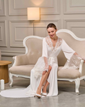 Bride sitting on vintage sofa wearing long lace robe with train and deep V-neckline, serene expression