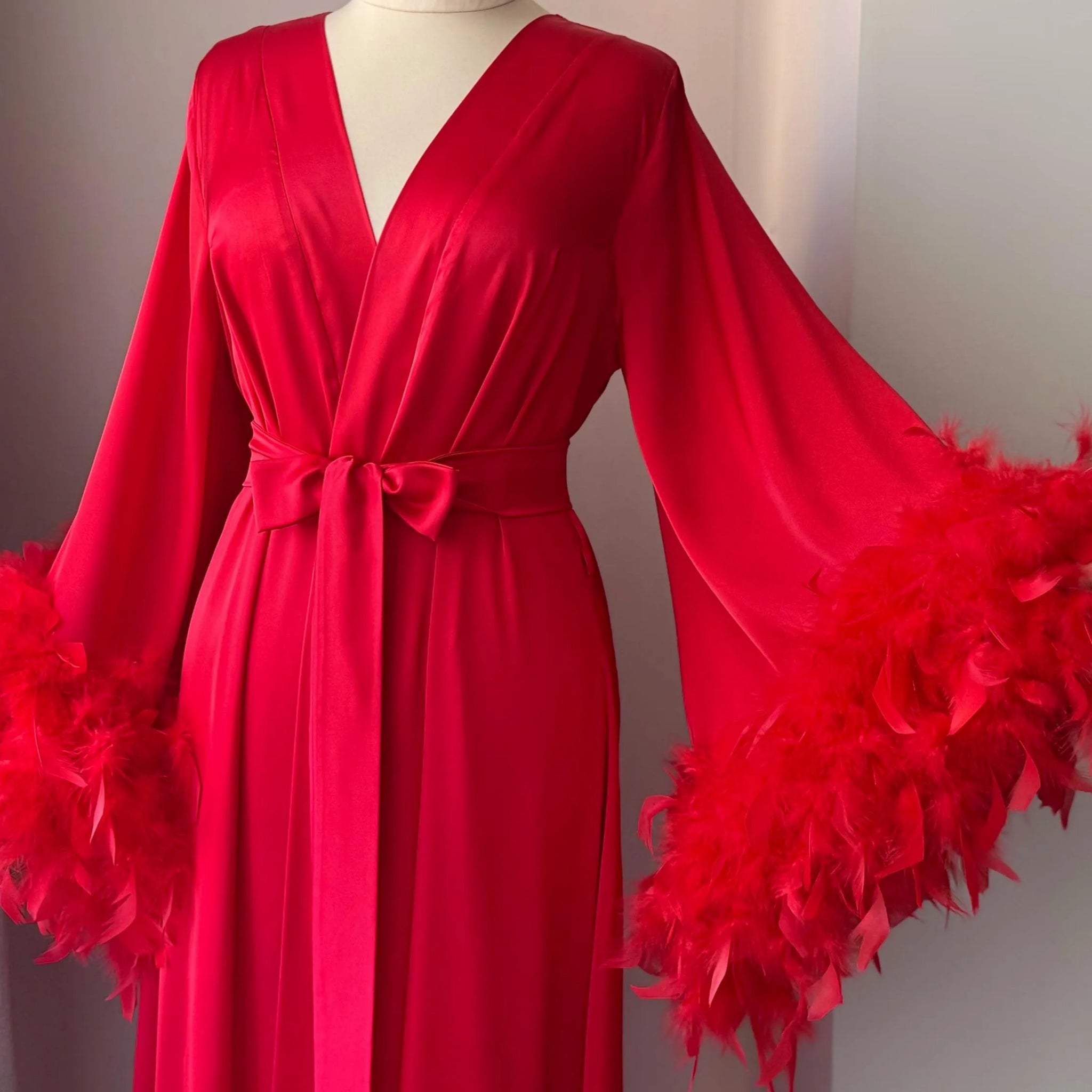 A red satin robe with long sleeves and feather accents, displayed on a mannequin.