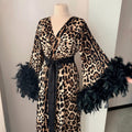 Leopard print satin robe with dramatic black feather cuffs and flowing long silhouette