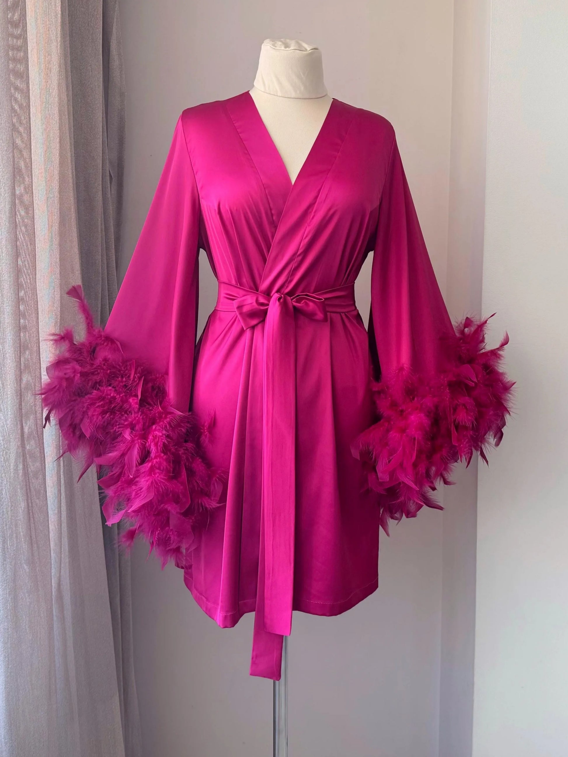 A bright pink satin robe with feather details, displayed on a mannequin.