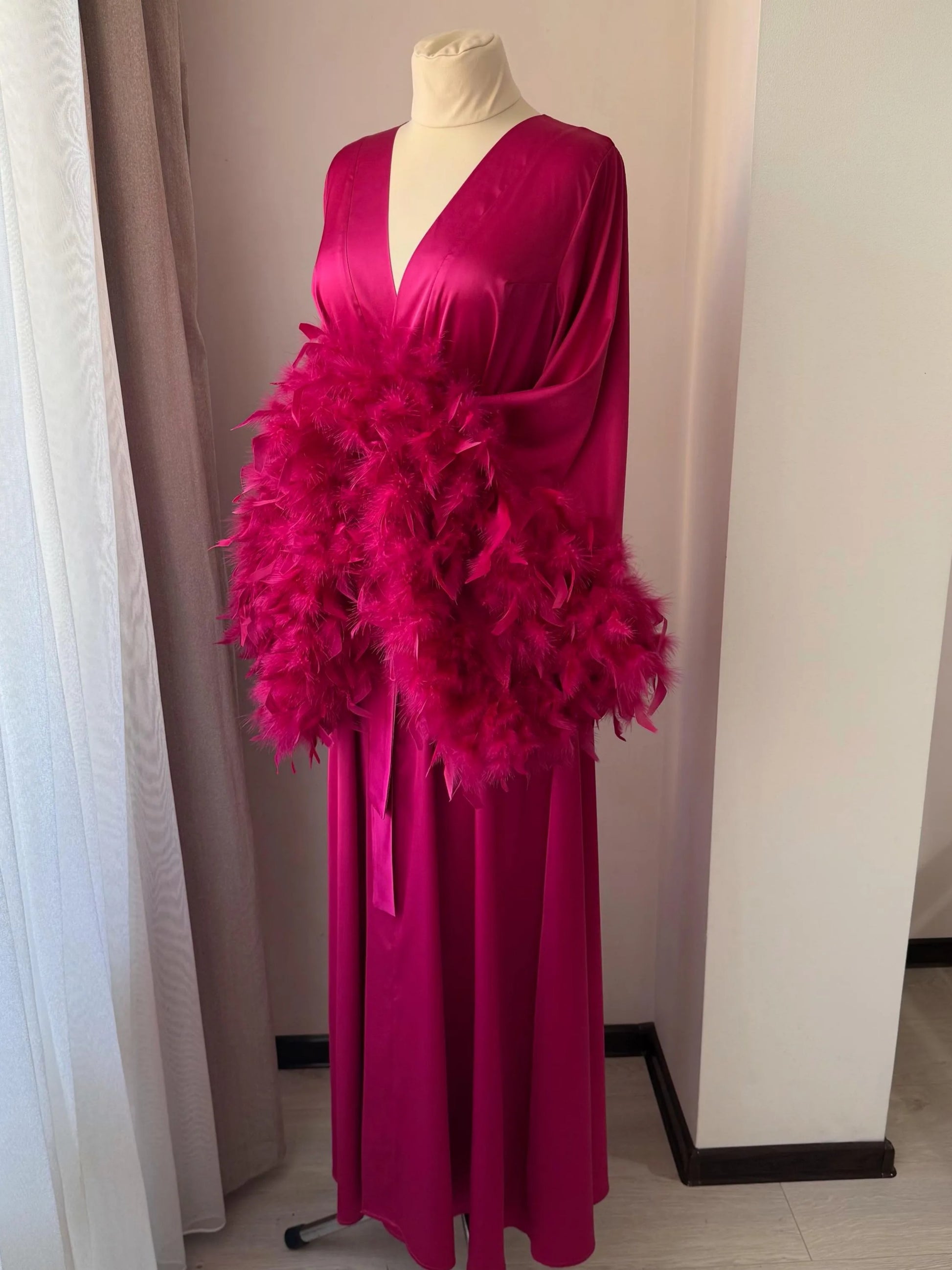 A mannequin wearing a long, pink dress with a large, fluffy feather accessory.