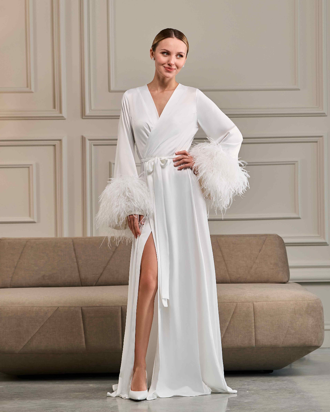 Side view of long ivory robe with ostrich feather details, model smiling in elegant bridal pose