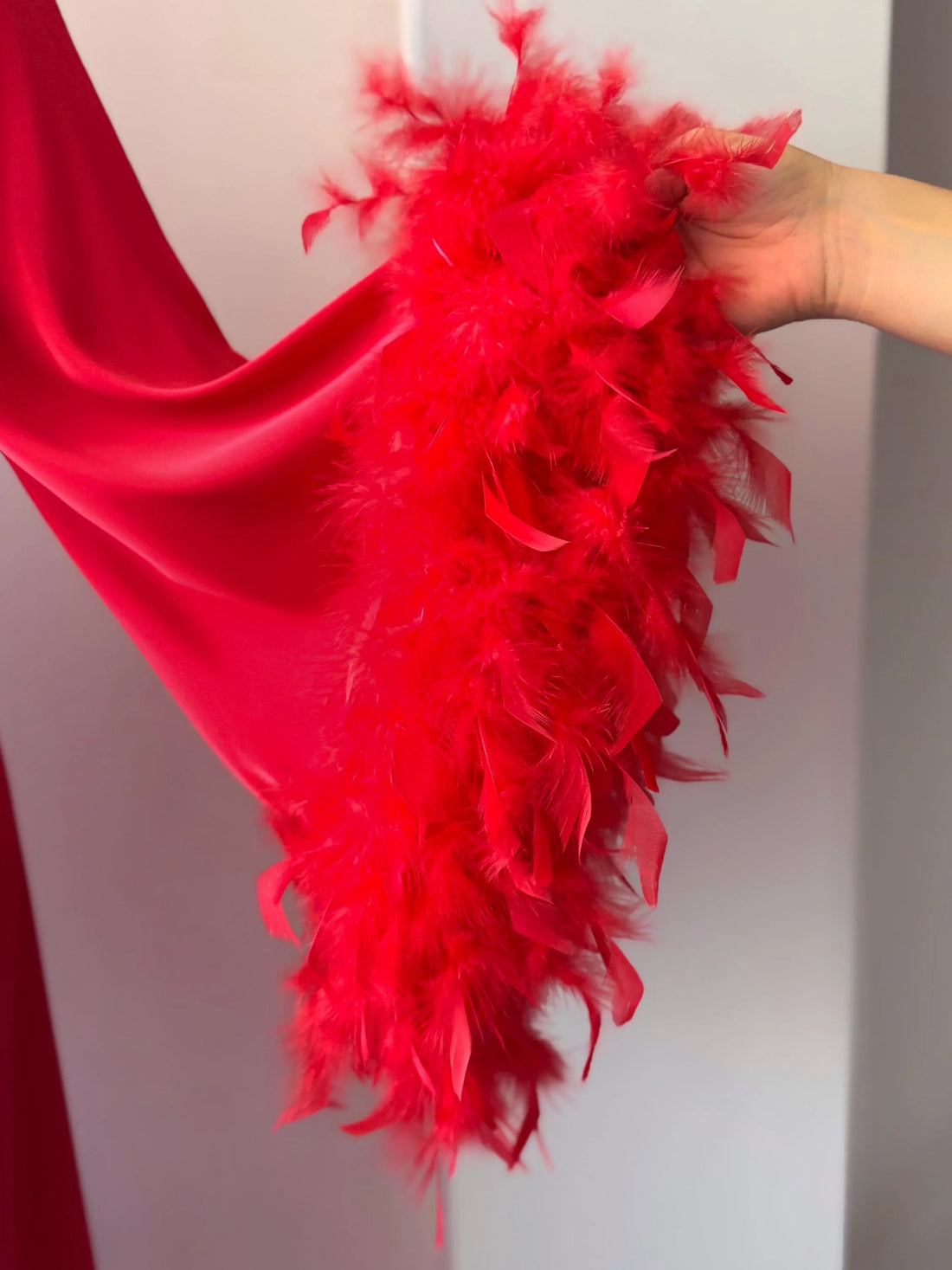 A red satin robe with long sleeves and feather accents, displayed on a mannequin.