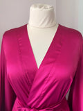 A mannequin wearing a bright pink satin robe with a white neckline and a white bust.