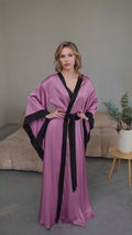 Video of flowing purple satin floor length robe with black trim on model