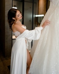 a bride in a white robe  looking at a wedding dress